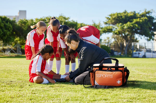 Junior girls football team and coach administering first aid 